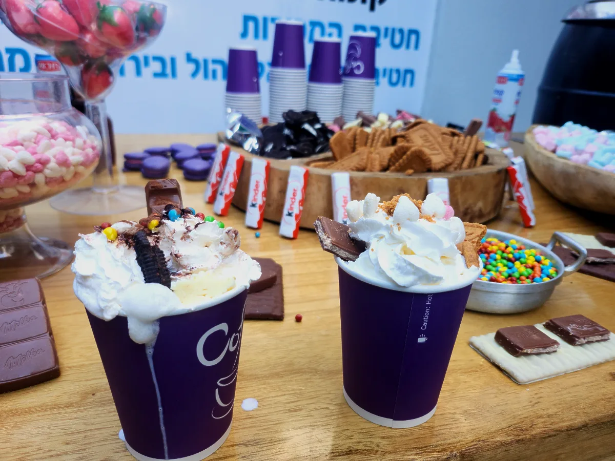 תקריב על כוס שוקו פינוקים עם הר של קצפת ופרלינים מלמעלה